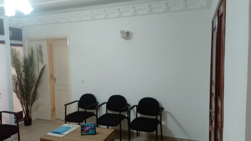 Hall d'accueil existant aux murs blancs avec sièges d'attente, avant transformation