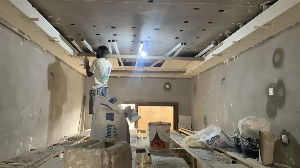 Pose en cours d’un faux plafond en staff dans un séjour, staffeur sur échafaudage