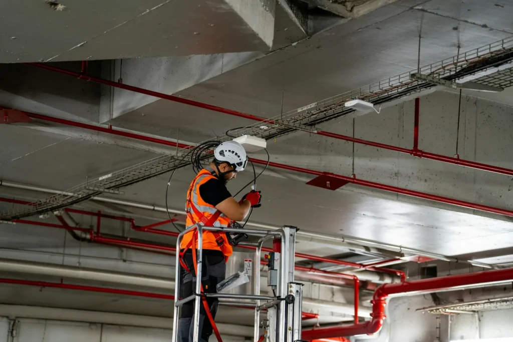 Technicien installant les réseaux électriques et de plomberie au plafond, lot MEP